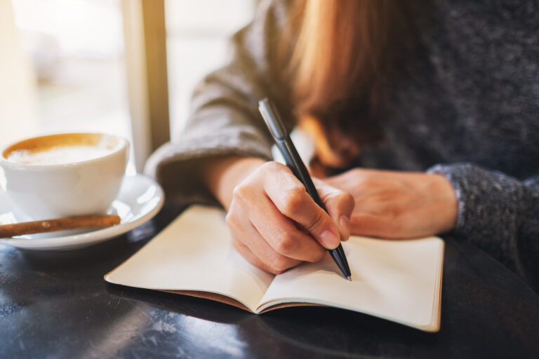 Closeup image of a woman writing on a blank notebook on the table